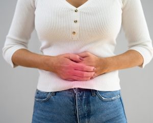 Kobieta z problemami flory bakteryjnej jelit, trzymająca brzuch z powodu odczuwanych dolegliwości